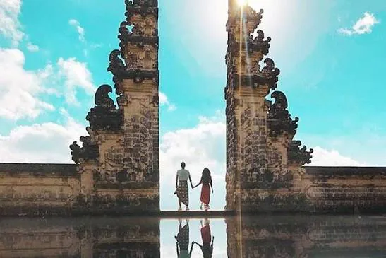 Two visitors framed by the tall stone gate at Besakih Temple against a bright sky