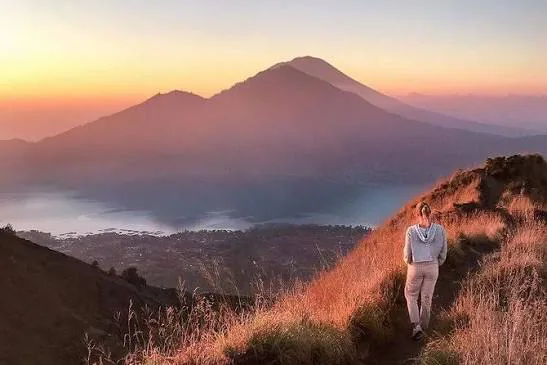 Sunrise over Mount Batur with a hiker on the ridge above the volcanic caldera