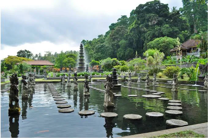 Tirta Gangga water palace with stepping stones, statues and a lush hillside backdrop