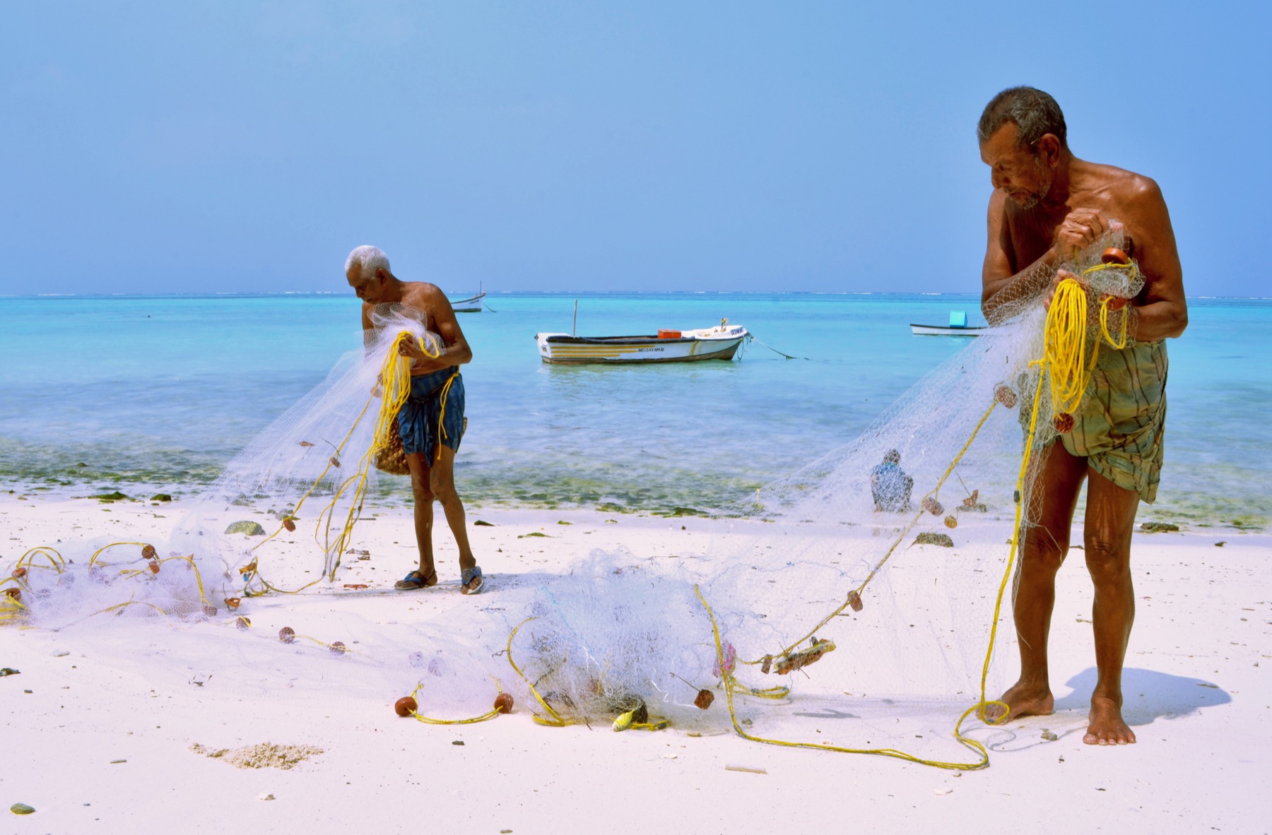 Fishers tending nets beside a bright Lakshadweep lagoon